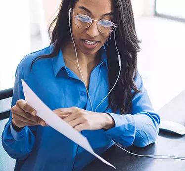 Women looking at a piece of paper with ear phones, wearing a blue long sleeve shirt 